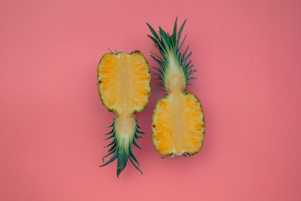 Freshly sliced pineapple halves on a vivid pink background, showcasing tropical vibes.